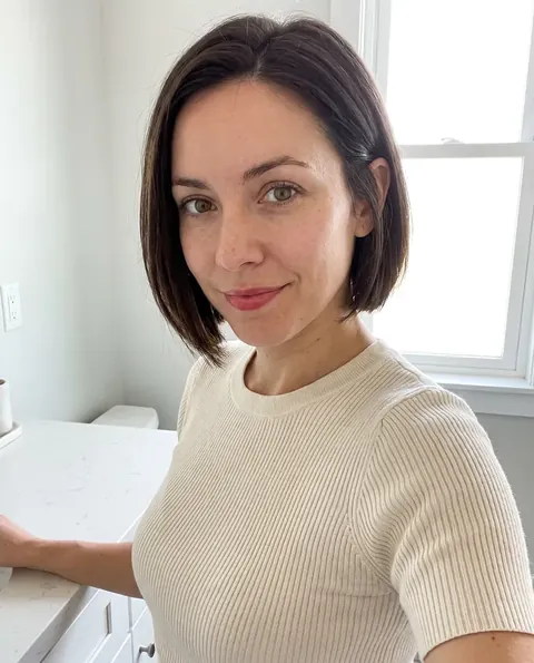 Nora, AI presenter, in a cream knit top